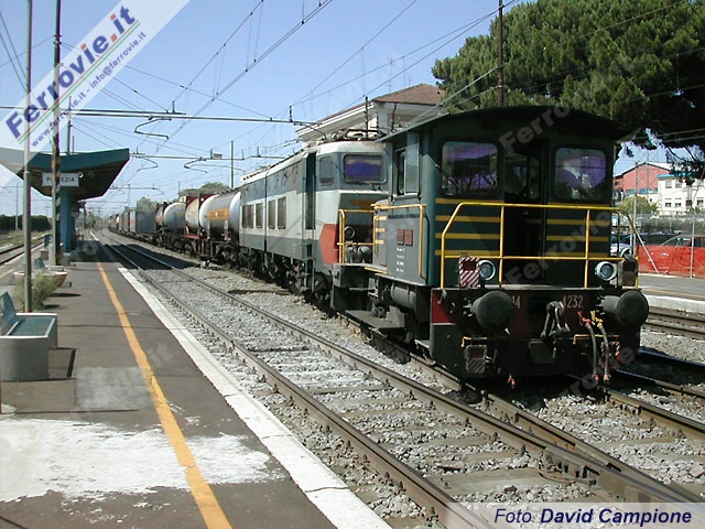 Lo scalo di Pomezia - S.Palomba vanta un discreto traffico merci, a servizio delle numerose industrie di zona. La 214.4232 sta liberando il binario di precedenza, manovrando un treno merci completo di locomotiva E.655. Il trasferimento del convoglio nello scalo adiacente (ubicato lato Formia) richiede l'attraversamento del binario di corsa pari.